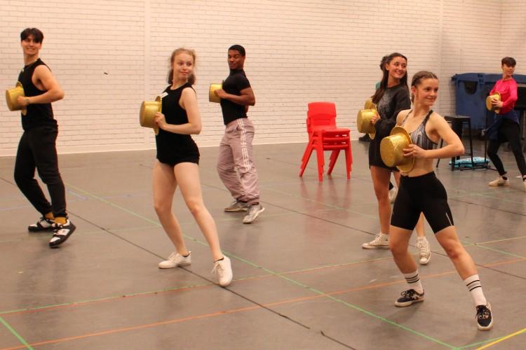 Students holding golden top hats rehearsing a musical